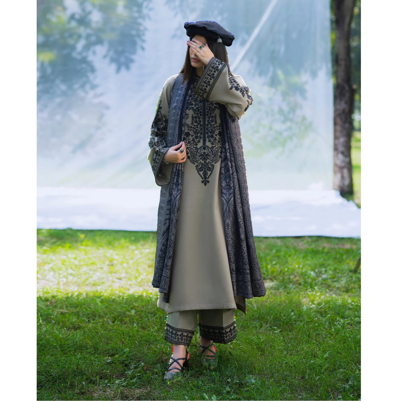 Person wearing a traditional outfit with a long embroidered jacket in an outdoor setting.